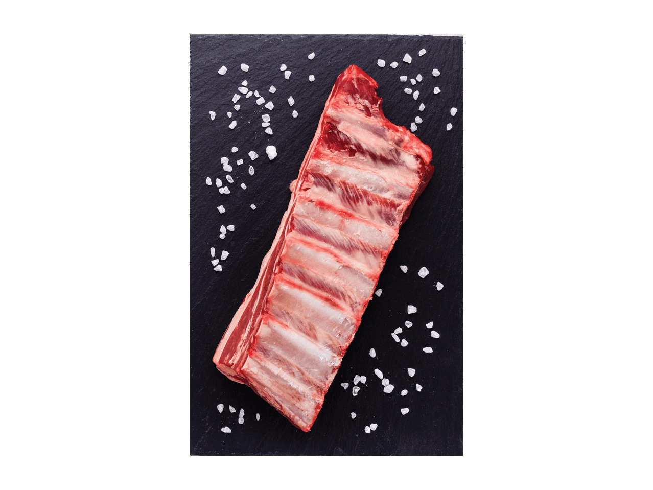 Švieži kiaulienos šonkauliai su druska ant juodos lentos.