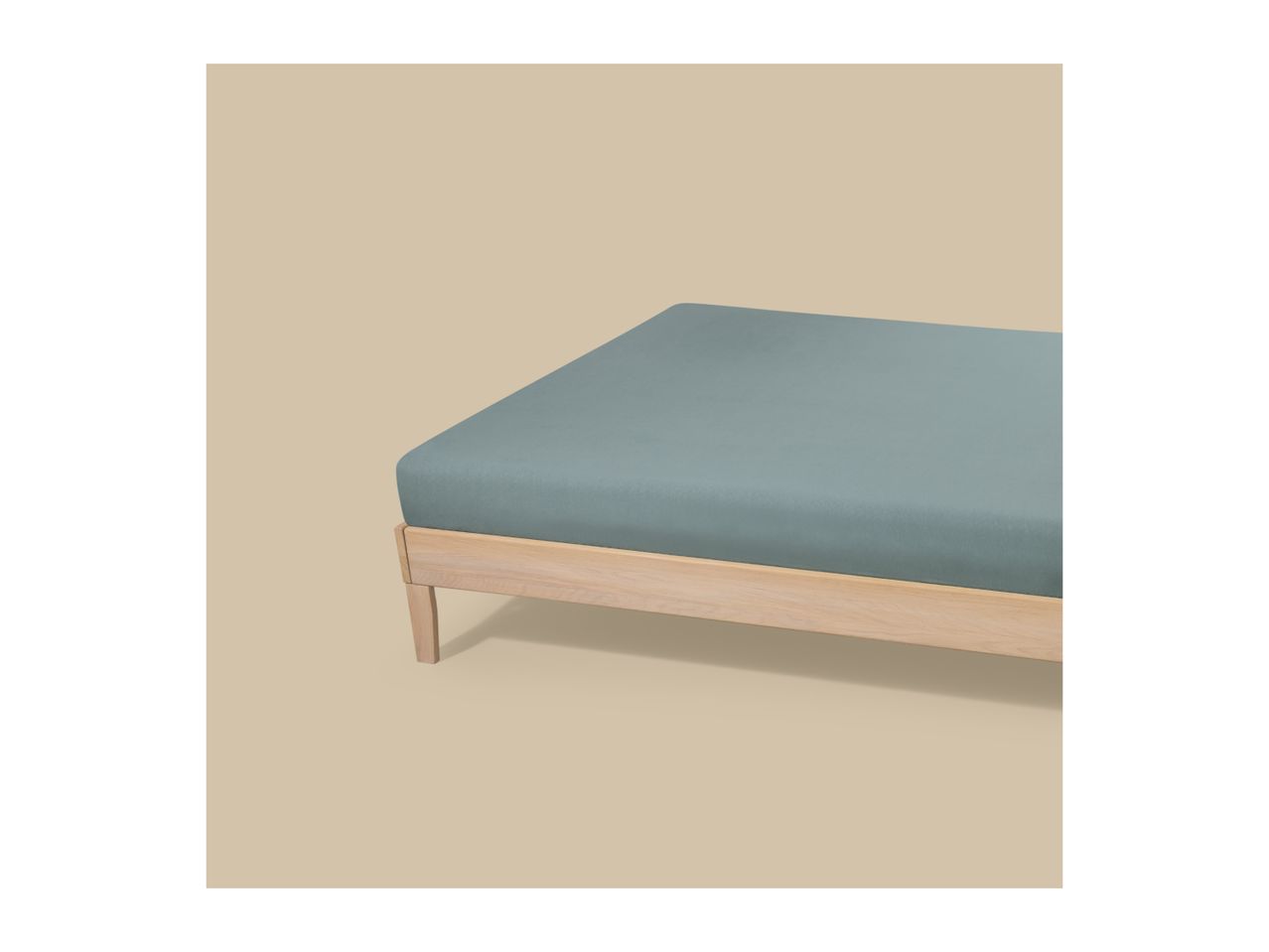 A light wooden bed frame with a fitted blue-green sheet on a beige background.