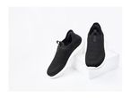 Pair of black slip-on sneakers with white soles, one standing on a white block.