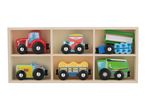 Wooden toy farm vehicles, including tractors, a seeder, a hay wagon, and a tipper, in a wooden box.