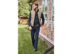 Man wearing an esmara® reversible gilet, plaid shirt, and jeans, walking past a brick house.