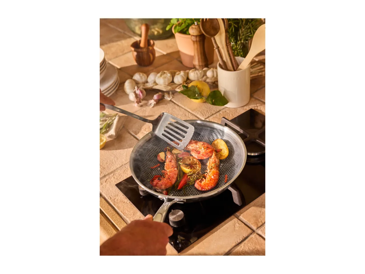 Cooking prawns with lemon and herbs in a pan on a hob, with garlic nearby.