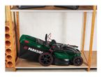 Folded green lawnmower with a black grass bag on a wooden shelf.