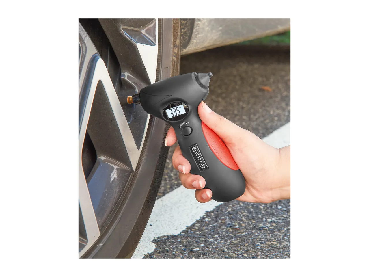 Hand holding a black and red Ultimate Speed tire pressure gauge on a car tire