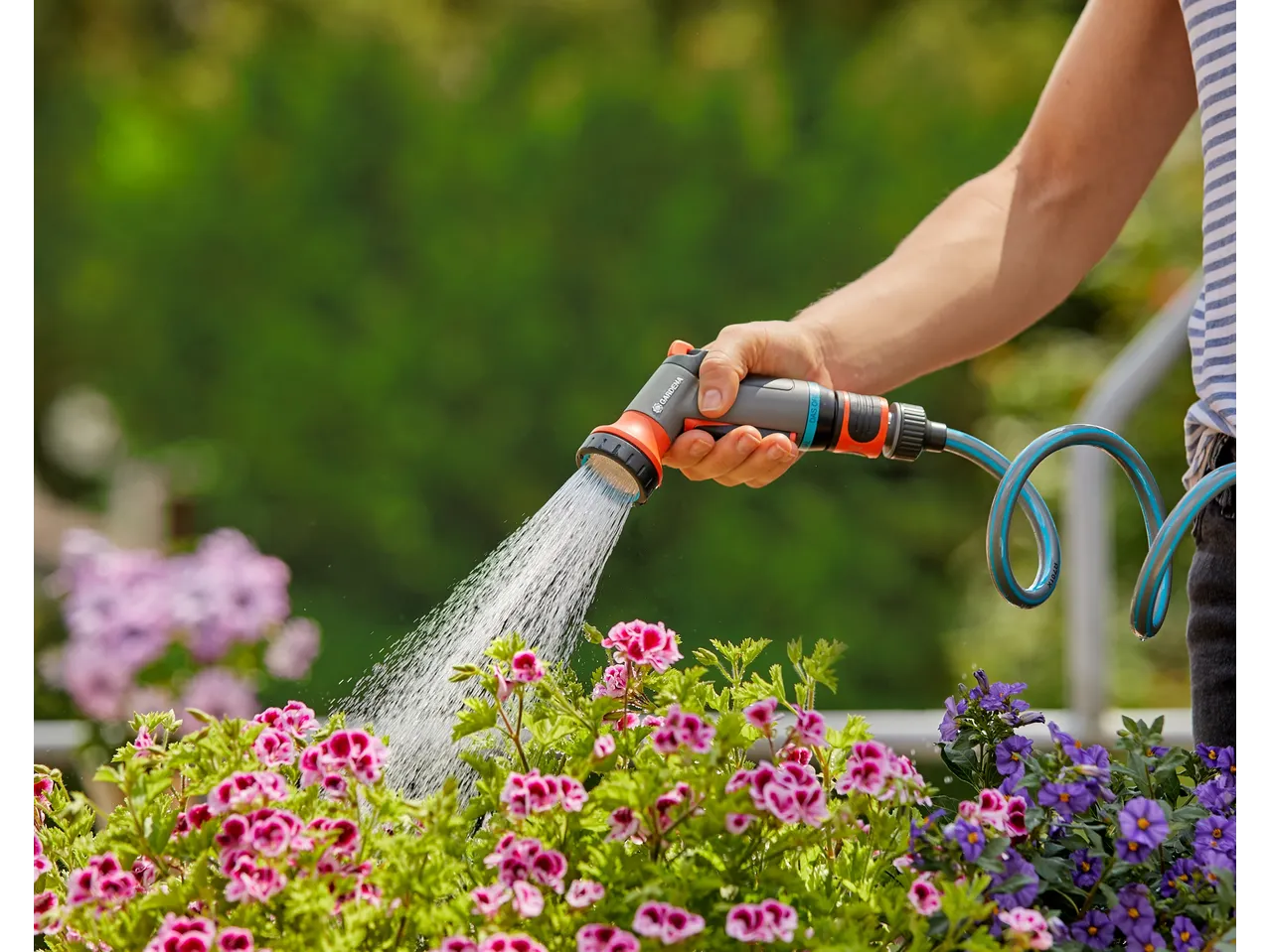 Χέρι ποτίζει λουλούδια με λάστιχο κήπου GARDENA.