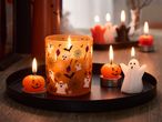Halloween-themed candles, including a ghost, pumpkins, and a jar with spooky decals, on a black tray.