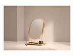 Gold oval vanity mirror with makeup pencil and small black container on a light surface.