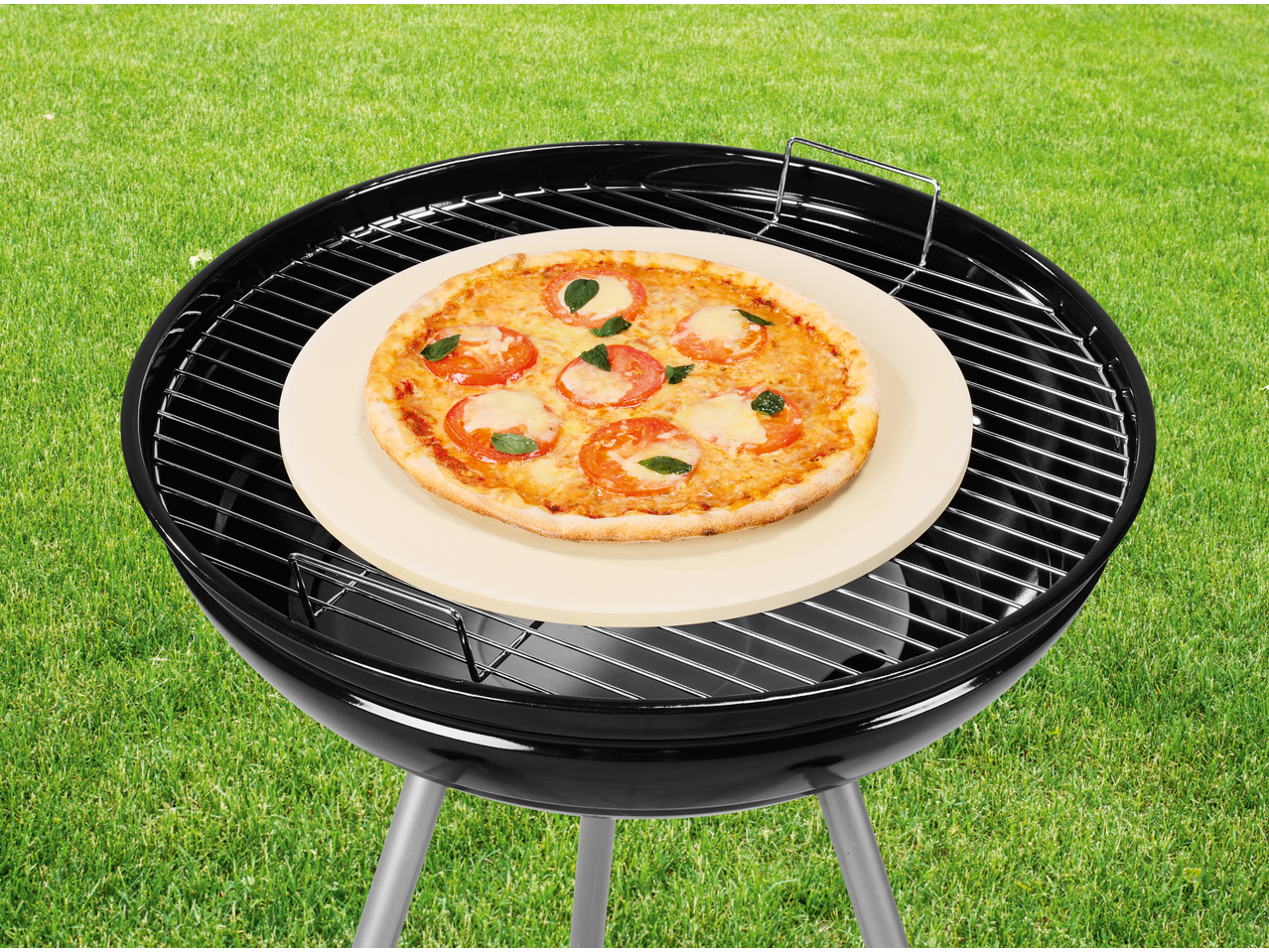 Piatră de pizza GRILLMEISTER cu pizza pe grătar, pe iarbă verde.