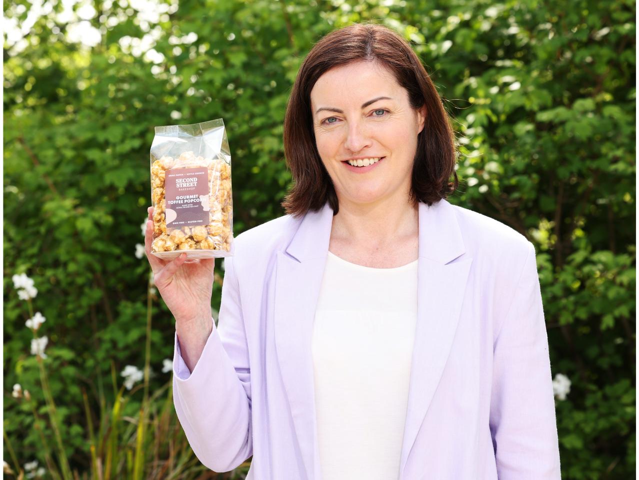 A woman holding a bag of Second Street Bakeshop Gourmet Toffee Popcorn.
