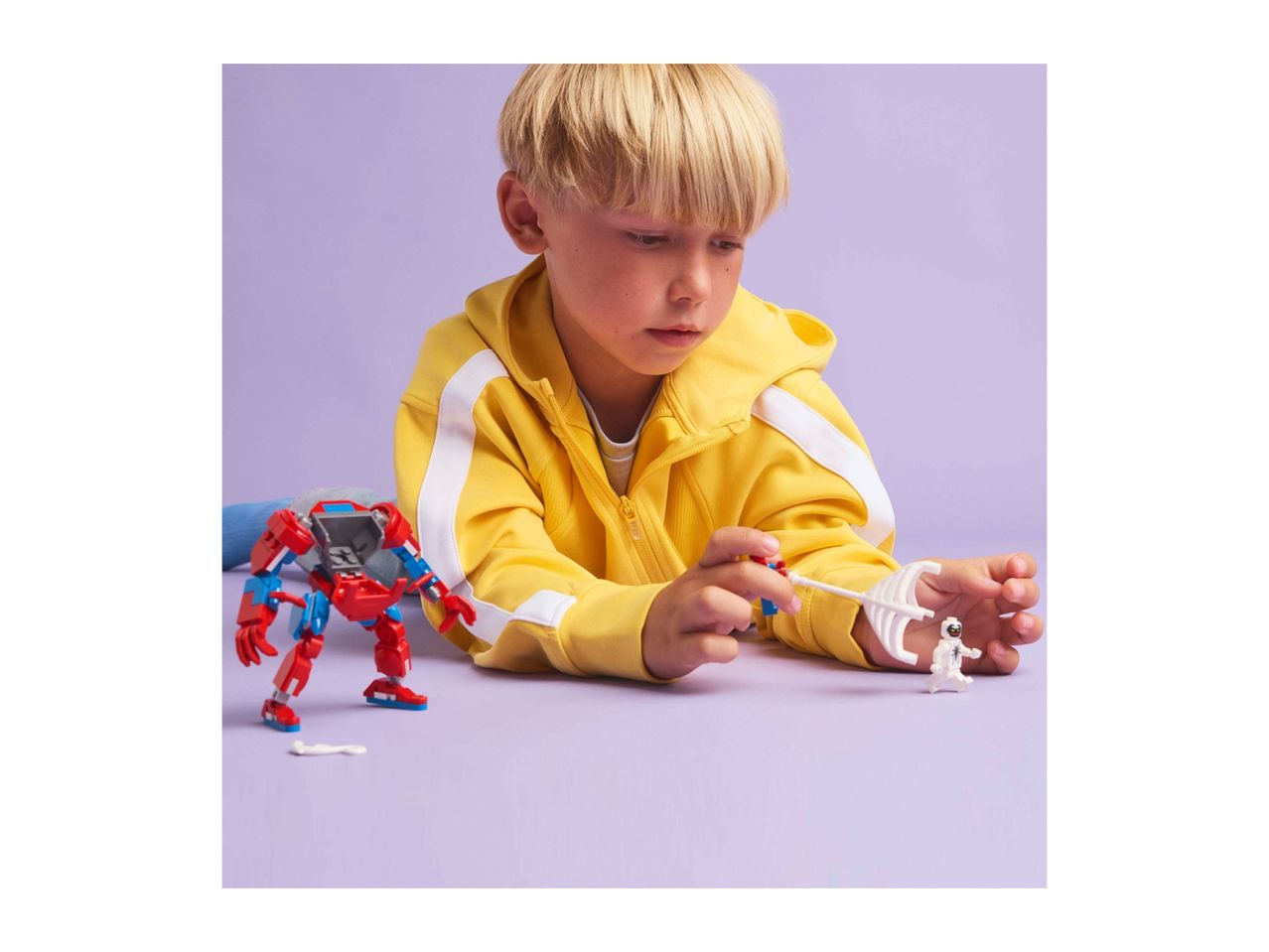 A child playing with a red and blue robot toy and a white astronaut figure.