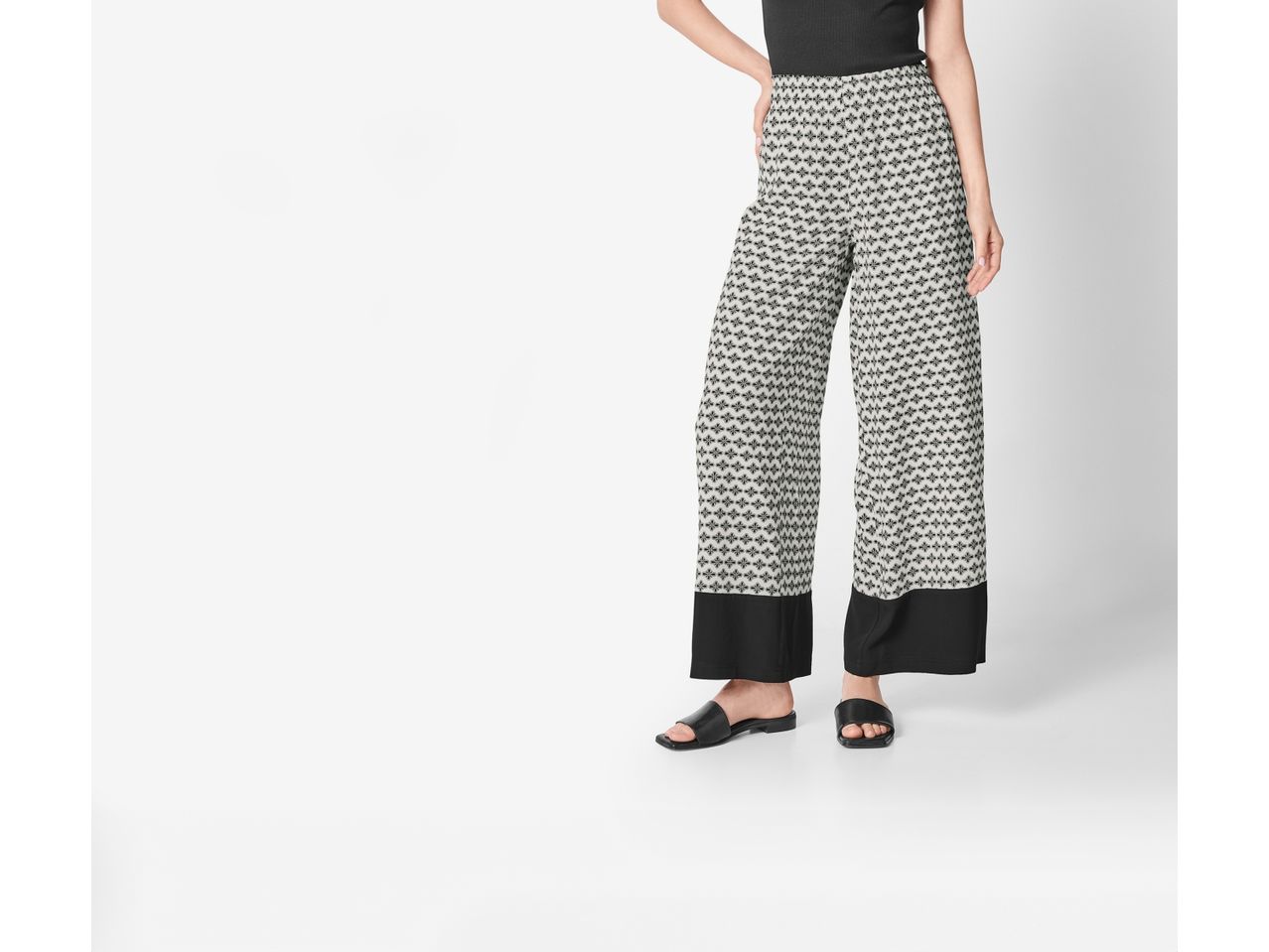 Woman wearing black and white patterned wide-leg pants and black sandals.