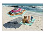 Woman reading on a striped beach mat under a colorful umbrella by the ocean.