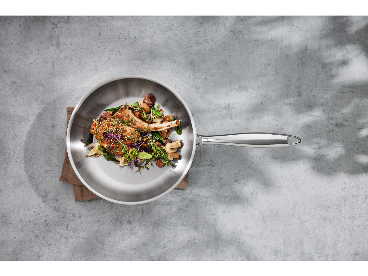 Vedere de sus a unei tigăi cu o cotletă de porc gătită, ciuperci și legume verzi.