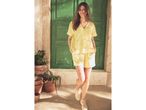 Woman in a yellow short-sleeved button-up shirt and matching shorts, smiling in front of a green door.