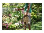 Person watering a garden with a hose and spray gun, holding coiled hose in other hand.