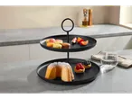 Un suport negru cu două etaje, cu prăjituri, macarons și fructe pe o masă de bucătărie.