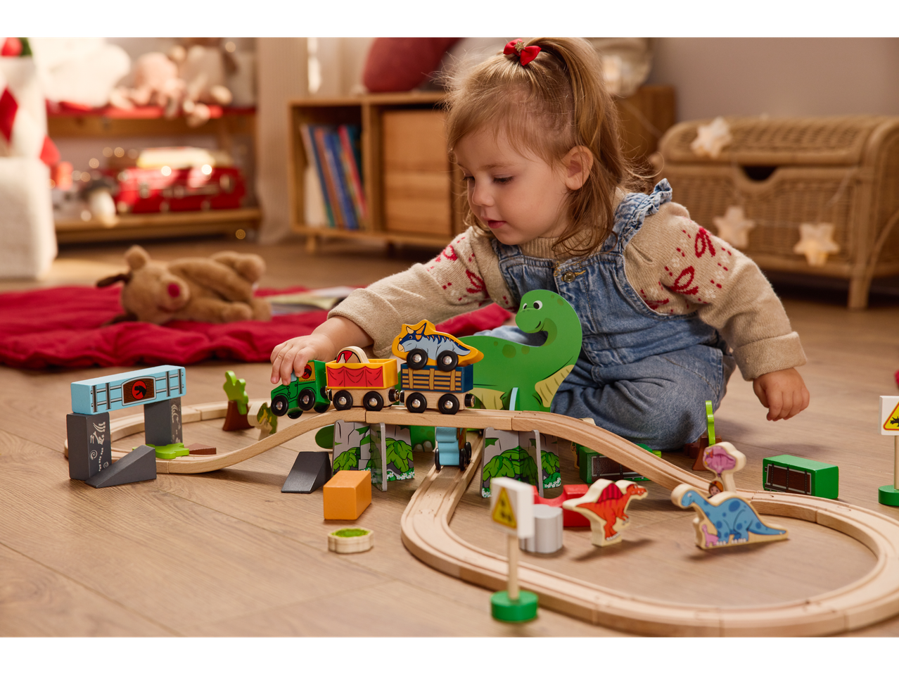Jeune enfant jouant avec un train en bois sur le thème des dinosaures sur le sol.