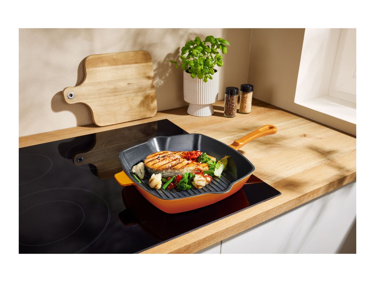 A grilled salmon and vegetables in a grill pan on an induction cooktop.