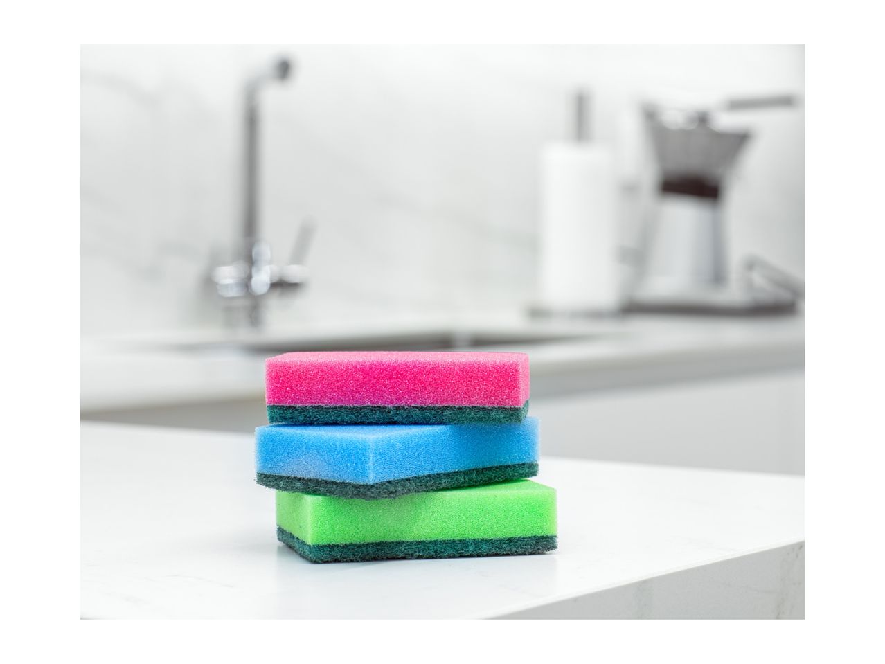 Stack of three colorful kitchen sponges on a white countertop.