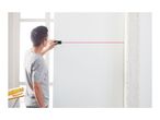 Man using a laser level to project a red line on a white wall.