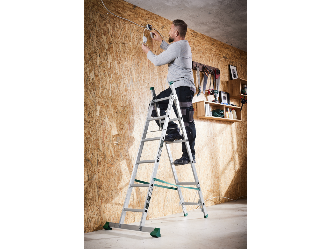 Man on a ladder installing electrical wiring on a wooden wall.