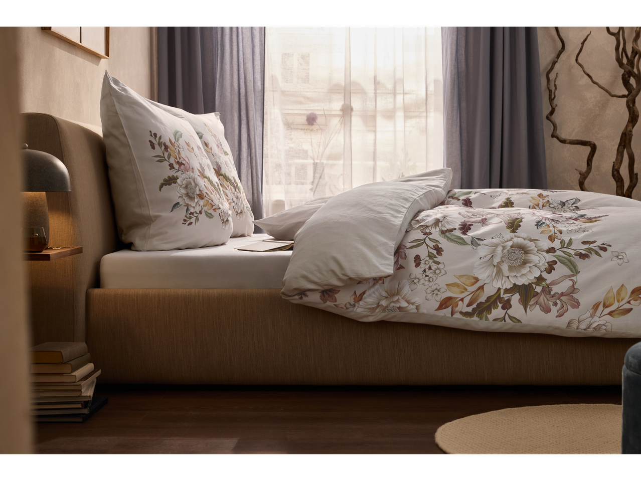 A beige bed with floral bedding sits near a window, showcasing a calm and sophisticated bedroom setting.