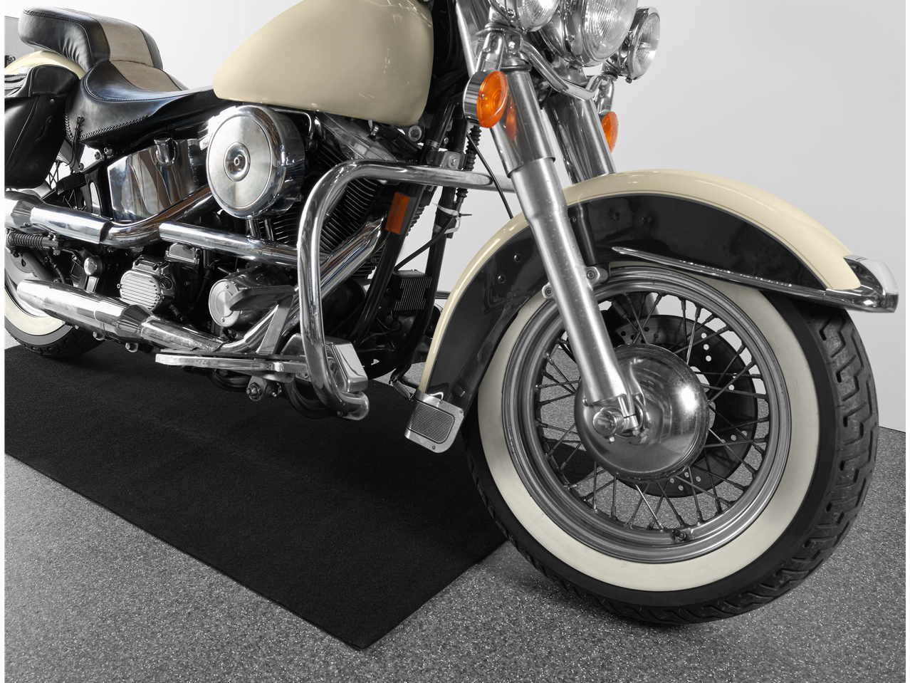 A cream and black motorcycle with chrome details and white sidewall tires sits on a black mat.