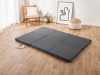 A dark gray foldable mattress on a light wood floor in a minimalist room.