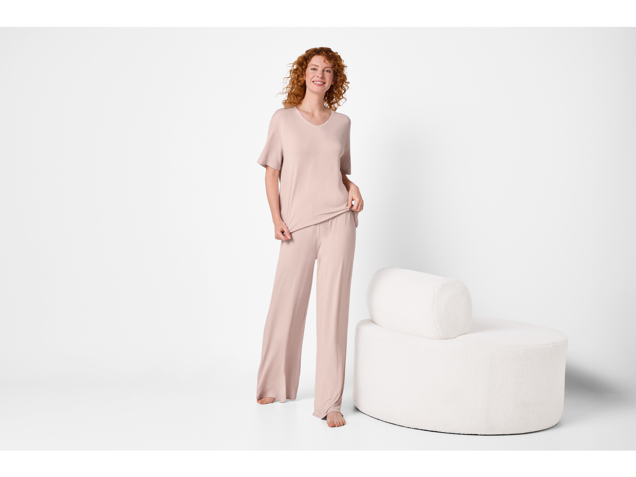 Woman in a light pink loungewear set, standing next to a white round armchair.