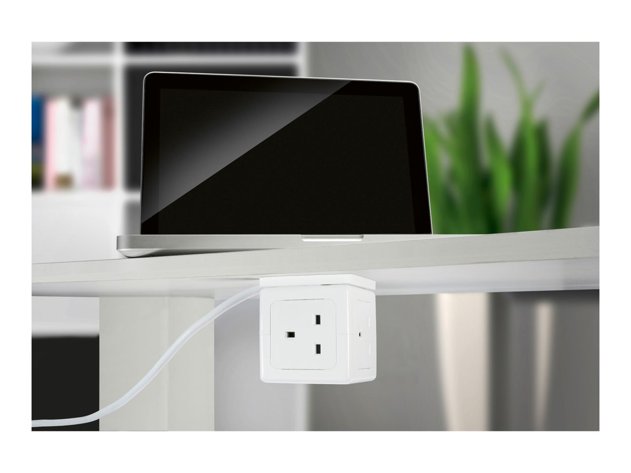 Laptop on a desk with a white power strip attached underneath, plugged into a cable.