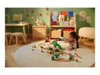 A child plays with a wooden dinosaur train set on a rug in a Christmas-decorated room.