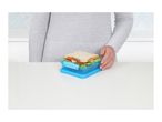 Person holding a blue sandwich container with a sandwich inside on a white table.