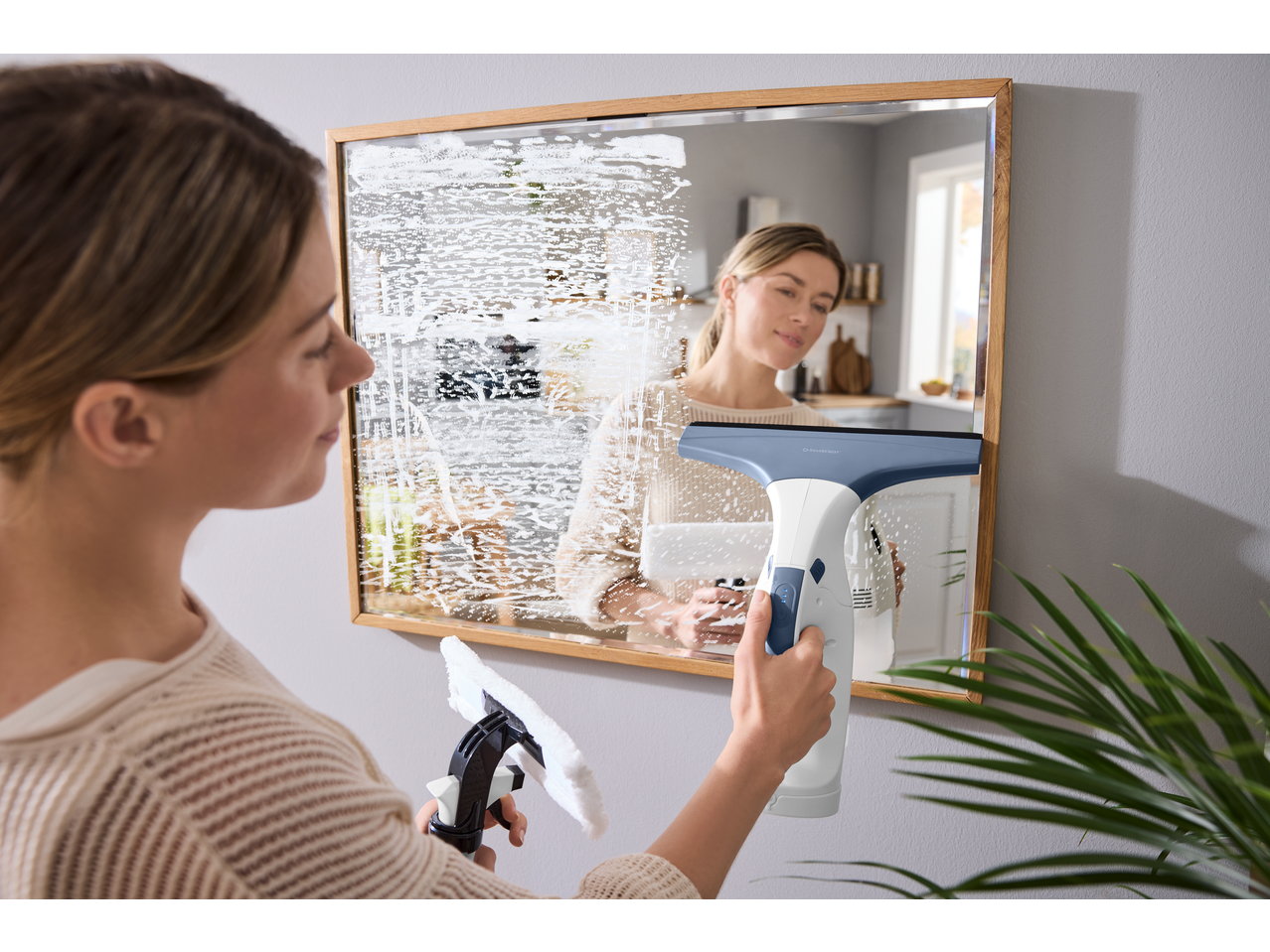 Woman cleaning a mirror with a spray bottle and a window vacuum cleaner.