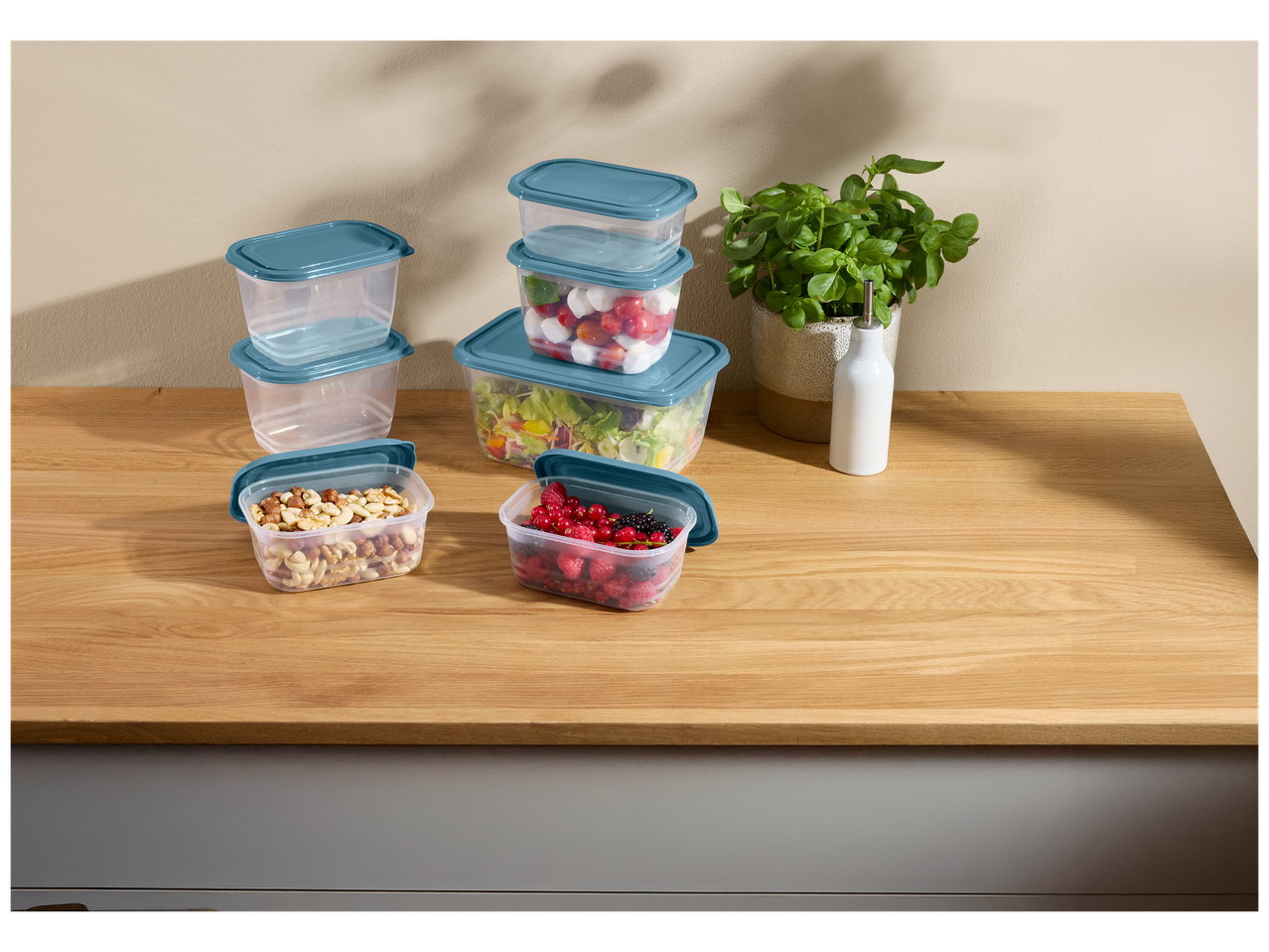 Boîtes de conservation transparentes avec couvercles bleus, remplies de salade, fruits et noix.