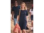 Uma mulher com um vestido de camiseta azul-marinho carrega uma bolsa de praia e uma toalha.