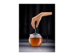 Hand pressing down a tea infuser into a glass teapot filled with amber tea.