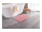 A pink bath mat on a gray tiled floor next to a white bathtub.