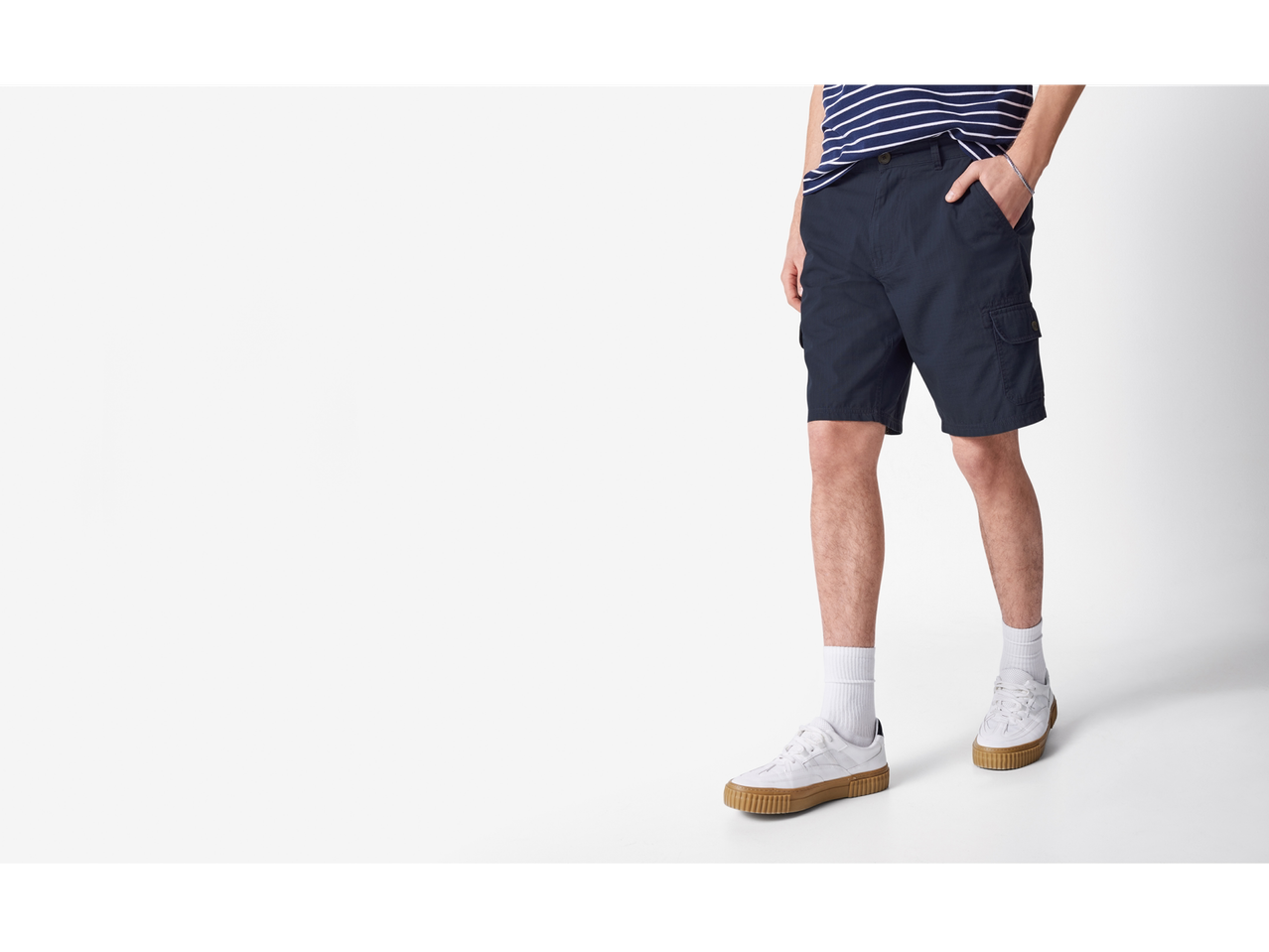 Un bărbat poartă pantaloni scurți cargo bleumarin și adidași albi.