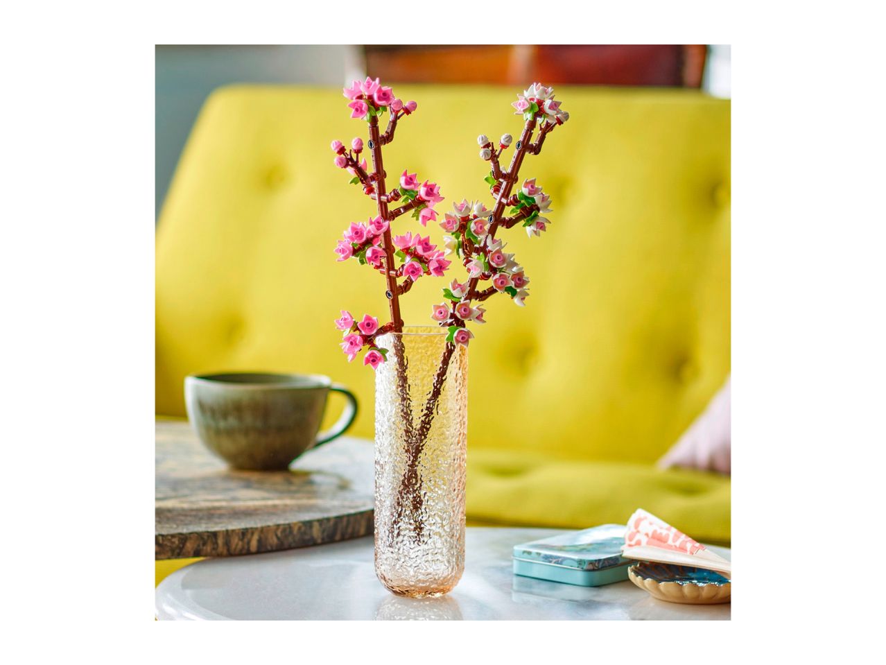 Pink and white artificial cherry blossoms in a textured glass vase on a table.