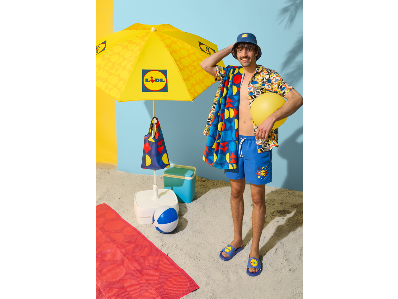 Man in Lidl short sleeve shirt, swim shorts, and bucket hat, with Lidl beach gear.