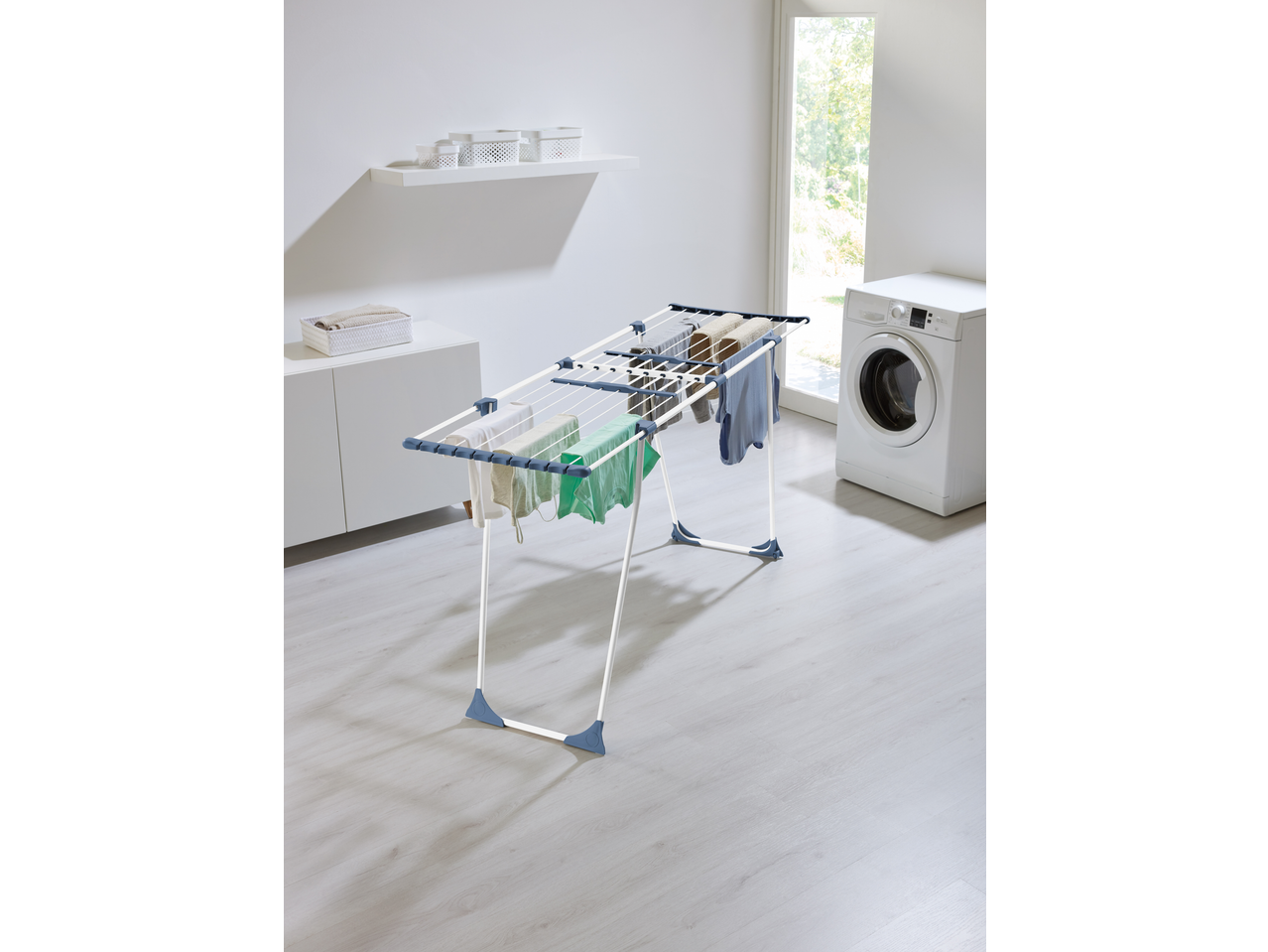 Laundry room with a clothes drying rack full of clothes, a washing machine, and storage.