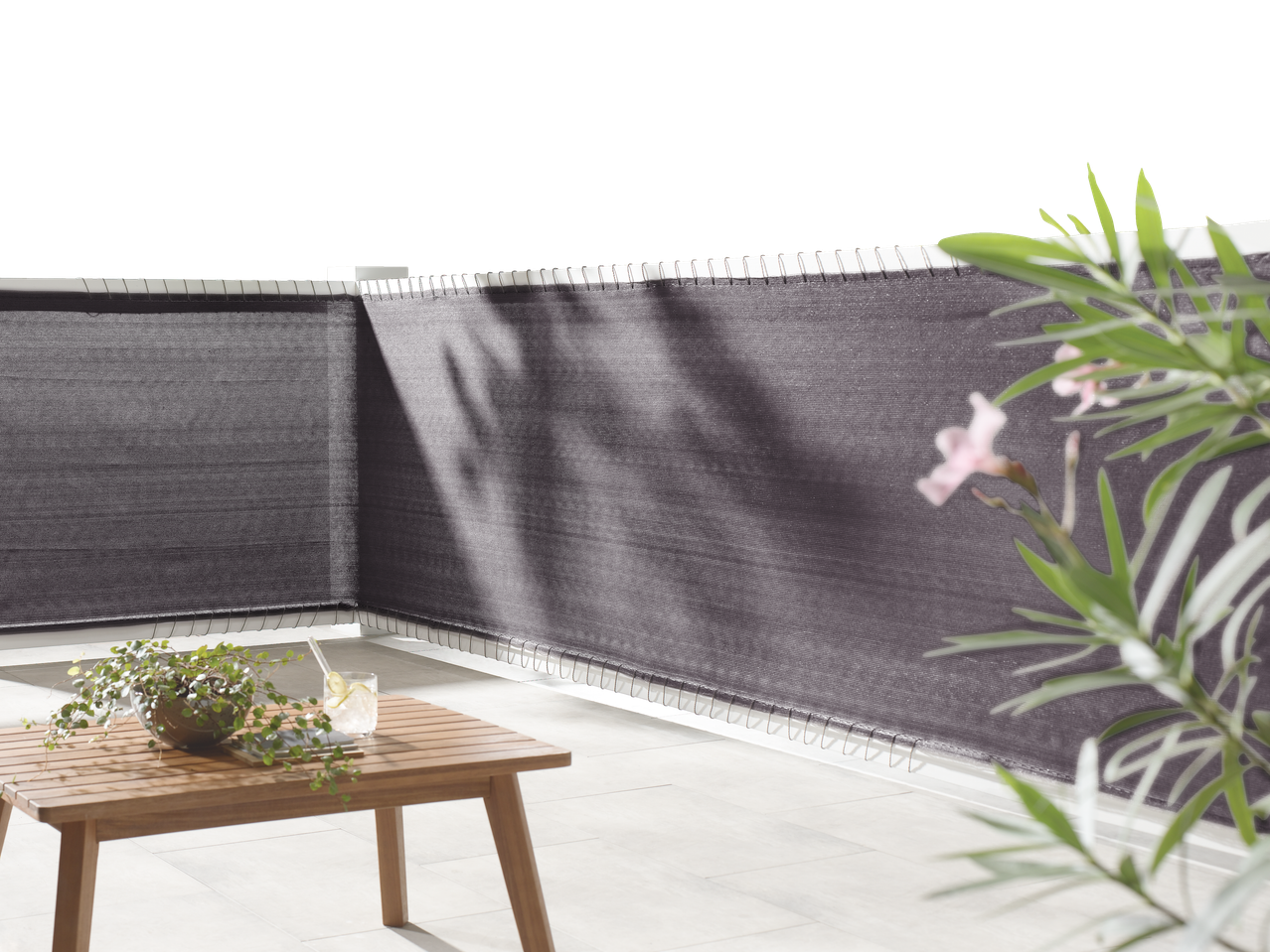 Balcon cu ecran de confidențialitate gri, masă din lemn și plantă.