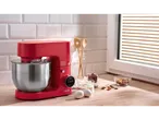 Red stand mixer with stainless steel bowl, baking ingredients on a wooden countertop