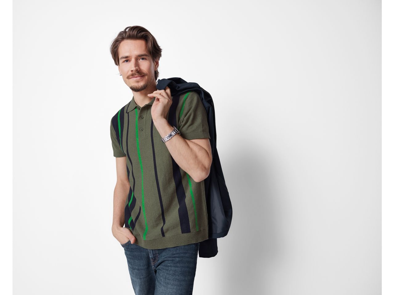 Uomo che indossa una t-shirt verde oliva a righe nere e verde acceso e un giubbotto nero.
