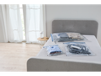 Vacuum storage bags with clothes on a bed, with a white lamp on a side table.