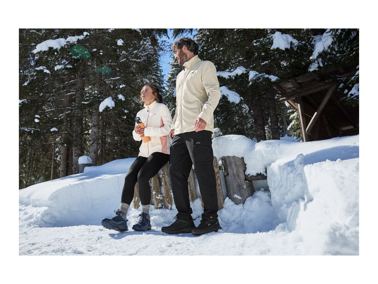 A man and a woman in warm winter clothing standing in a snowy forest.