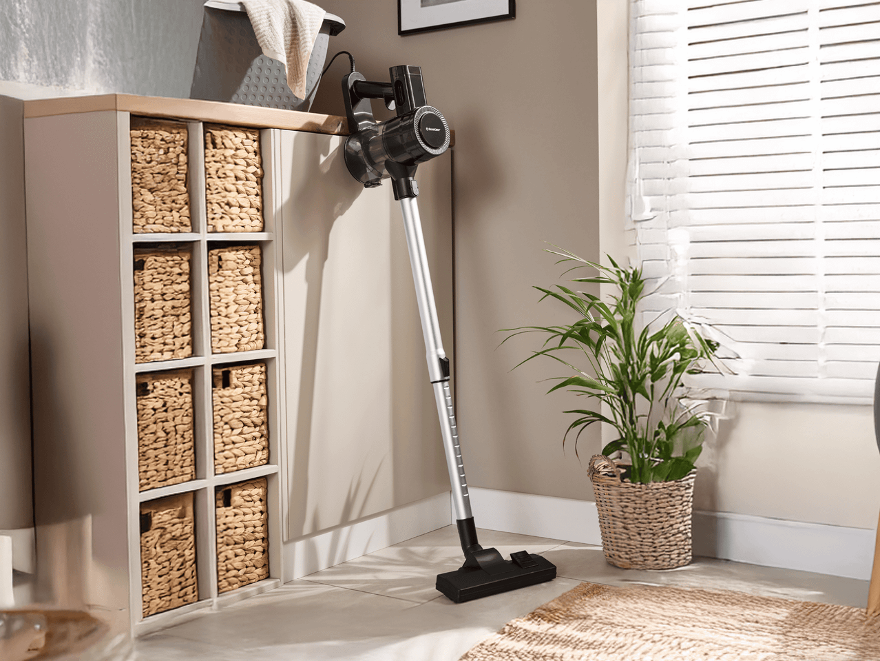 Silvercrest Akku-Stielstaubsauger an der Wand montiert, neben einem Regal mit Körben und einer Pflanze.