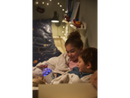 Duas crianças aconchegadas em cobertores macios assistem a um projetor de estrelas.