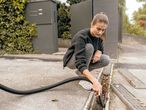 A woman uses a wet/dry vacuum to clean leaves from a drain.