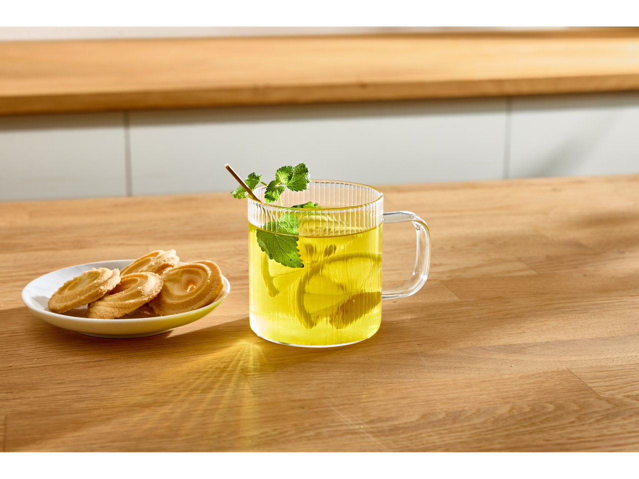 Cana de sticlă cu ceai de lămâie și mentă, lângă o farfurie cu biscuiți.